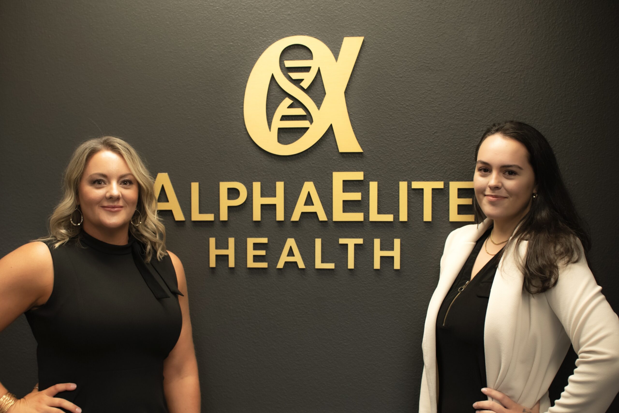 Two AlphaElite Health team members in front of the gold clinic logo